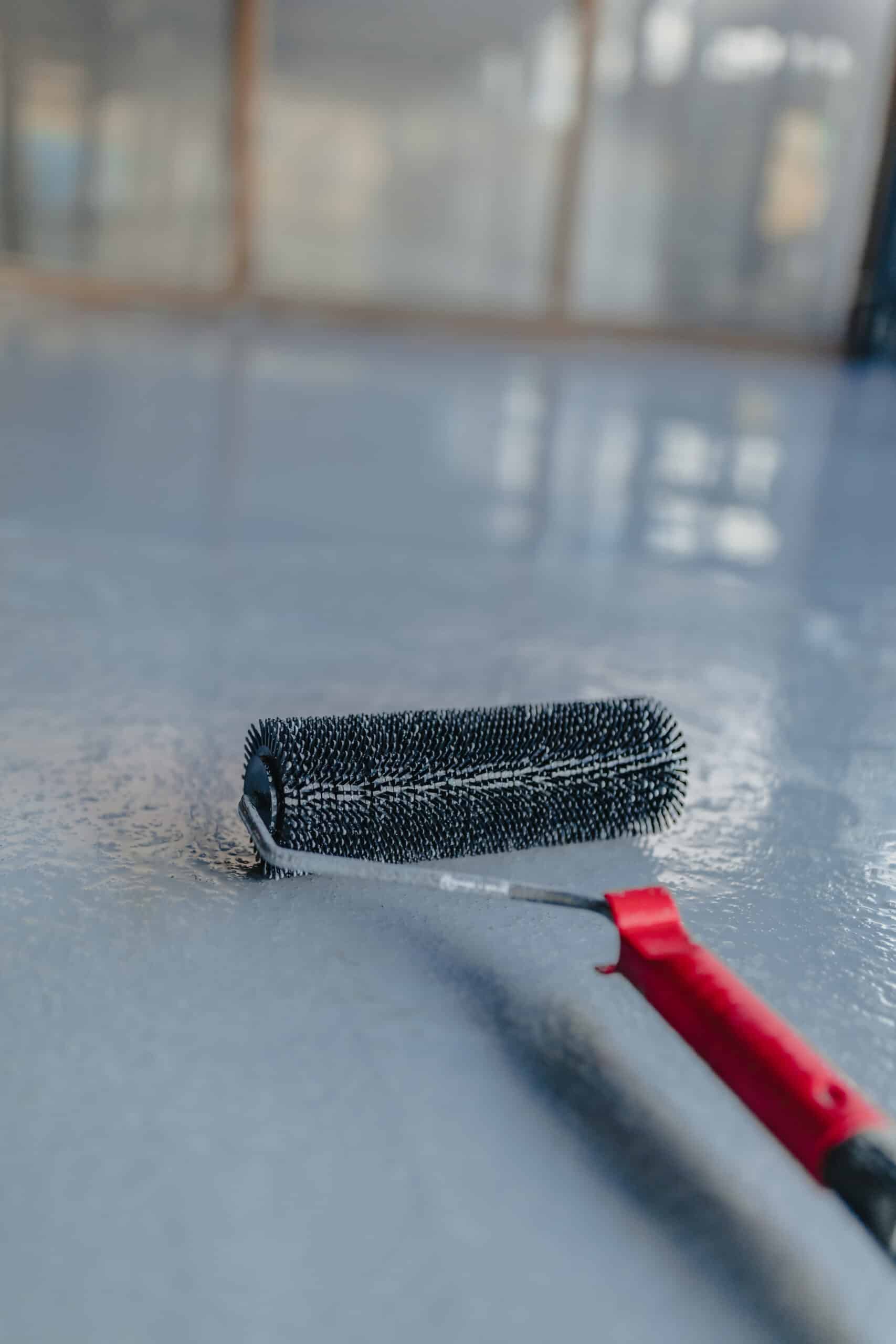 Spiked roller is used to evenly distribute resin on a gray industrial floor, creating a smooth and durable surface